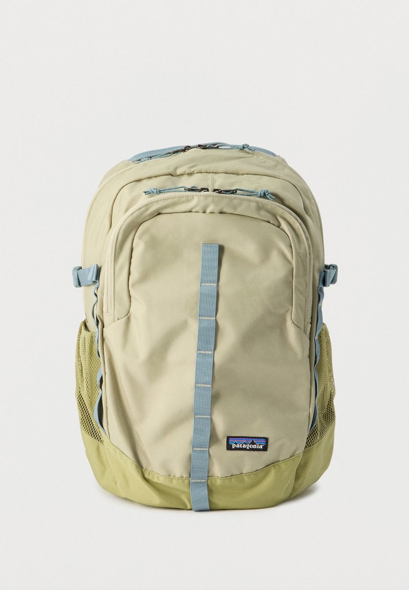 Μπεζ και ανοιχτοπράσινο σακίδιο Patagonia με πολλαπλές θήκες με φερμουάρ και μπλε κάθετο ιμάντα μπροστά, διχτυωτές πλαϊνές τσέπες.
