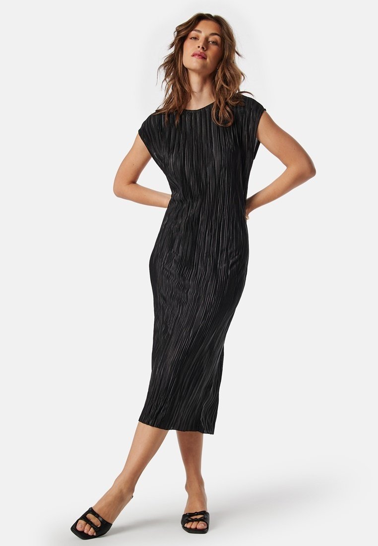 Czarna midi sukienka o plisowanej fakturze, z krótkimi rękawami i luźnym krojem. Dobrane do niej czarne sandały na otwartym palcu.