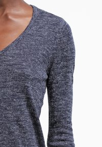 Suéter de punto gris oscuro con cuello en V, mangas largas y un patrón texturizado. Material suave con ligeras variaciones de color.