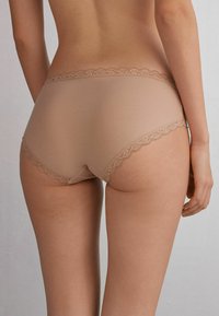 Beige katoenmix slip met een decoratieve geschulpte kantafwerking op de taille en benen, met een gladde textuur en een aansluitend ontwerp.