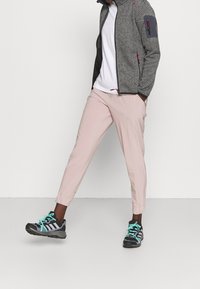 Szara teksturowana kurtka z czarnymi akcentami, biały t-shirt, jasnoróżowe zwężane spodnie oraz czarne sportowe buty z turkusowymi detalami.