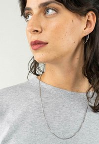 Zilveren ketting die over een grijze sweatshirt wordt gedragen, met een eenvoudig ontwerp, een gladde textuur en een lichte glans.