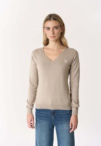 Maglione beige a scollo a V realizzato in tessuto morbido, con maniche lunghe e polsini a costine. Dettaglio ricamato sottile sul petto.