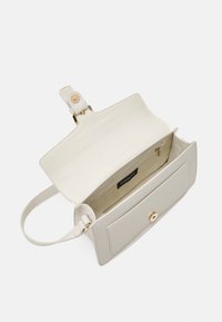 Sac à main en cuir gris clair avec une texture lisse, de la quincaillerie ton or et une seule bandoulière. L'intérieur présente une doublure crème et une poche zippée.