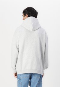 Sweatshirt à capuche gris avec une texture douce, des manches longues et une coupe décontractée. Il présente une grande capuche et un ourlet côtelé. Associé à un jean bleu.