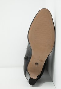 Chaussure en cuir noir avec un bout pointu, dessus texturé et semelle lisse. Présente un talon en caoutchouc et un logo de marque en relief sur la semelle intérieure.