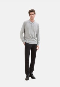 Lichtgrijze poloshirt met lange mouwen en een kraag, gecombineerd met zwarte broek en zwarte schoenen. Gladde textuur, eenvoudig ontwerp, geen patronen.