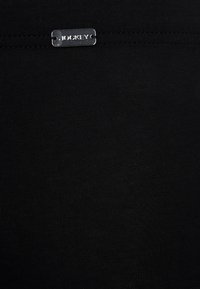 Czarna elastyczna tkanina o gładkiej fakturze, z metaliczną srebrną metką z logo "JOCKEY". Minimalistyczny design bez wyraźnych wzorów.