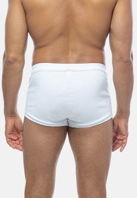 Costumi da bagno bianchi a coste con una cintura morbida, mostrati da dietro, caratterizzati da una vestibilità aderente e dettagli di cucitura minimi.