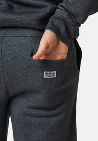 Szare dresowe spodnie z polaru z boczną kieszenią i białą metką na tylnej kieszeni, charakteryzujące się miękką teksturą i luźnym krojem.