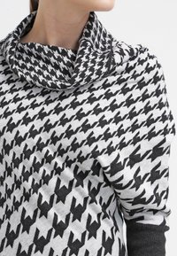 Sweter z wzorem pepitki w czarno-białe, z fakturą i golfem o luźnym kroju. Miękka tkanina, luźno dopasowana wokół ramion.