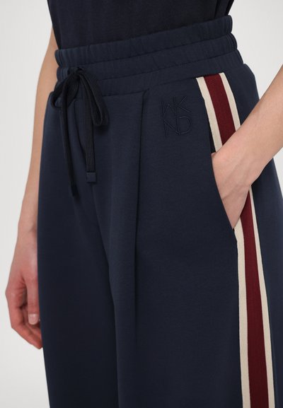 Navy joggers with a drawstring waist, featuring red and cream side stripes and embossed "WKND" logo. Material appears soft and textured.