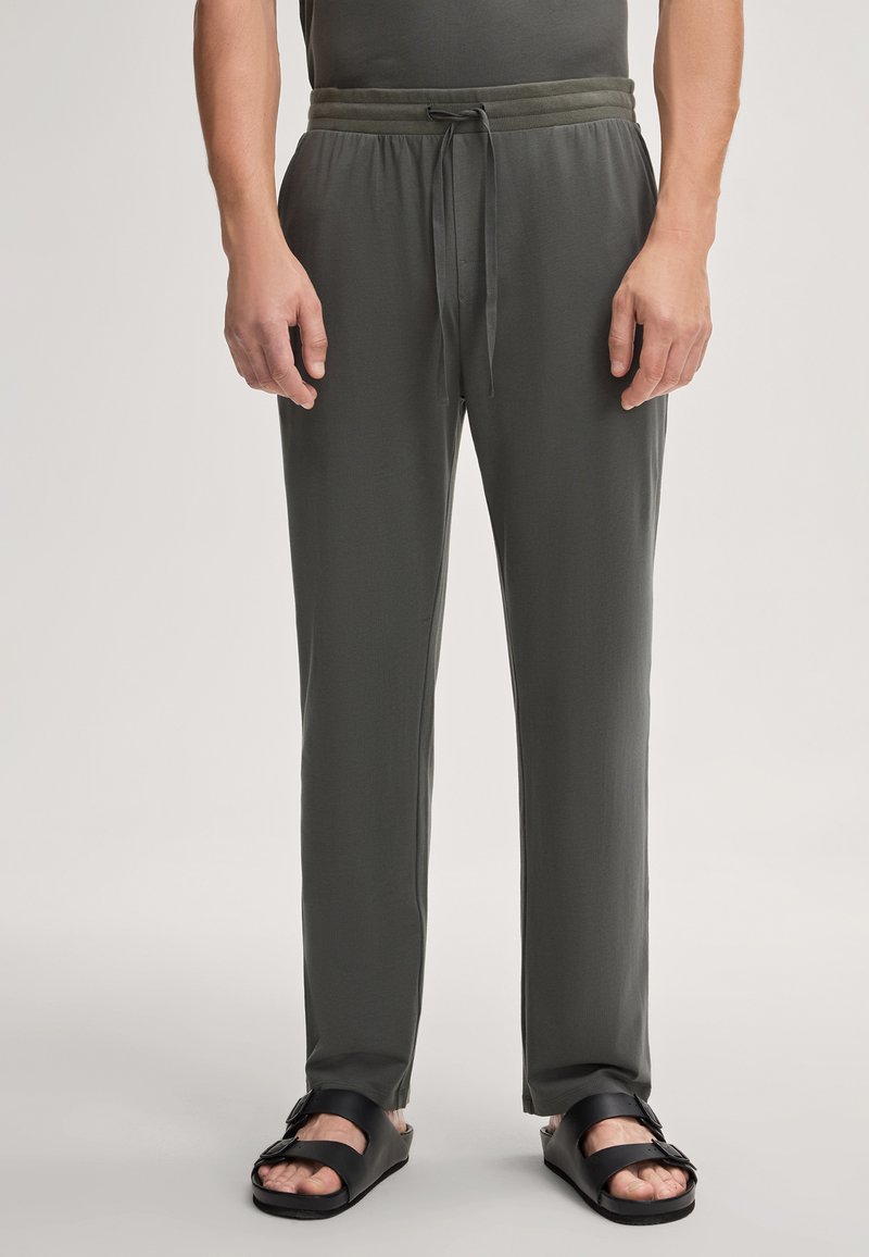 Leichte, dunkelgrüne Herren-Loungewear-Hosen mit elastischem Bund, Kordelzug und lockerer Passform, kombiniert mit schwarzen Sandalen.