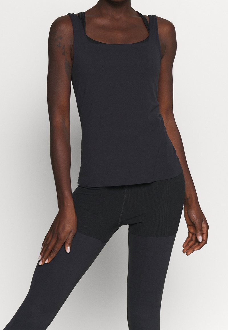 Black athletic tank top with a square neckline and wide straps, paired with black leggings featuring a textured panel design.