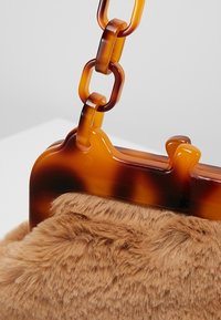 Gros plan d'un sac à main en fausse fourrure marron avec un fermoir en écaille de tortue et une chaîne épaisse en écaille de tortue sur un fond uni.