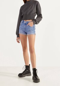 Grå kort sweatshirt med samlad midja, i kombination med ljusblå denimshorts med upprullade fållar och slitningar. Svarta snörstövlar.