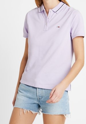 Liliowa koszulka polo z kołnierzykiem, trzema guzikami i małym logo. W połączeniu z jasnoniebieskimi szortami jeansowymi z postrzępionym brzegiem.