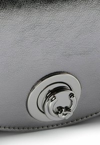 Borsa in pelle grigia con superficie testurizzata, forma arrotondata e una fibbia circolare argento lucido con un design dettagliato.