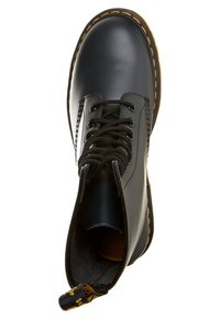 Bota de tobillo de cuero negro con punta redonda, cordones negros y costuras amarillas a lo largo de la suela. Cuenta con una pestaña en el talón para facilitar su uso.