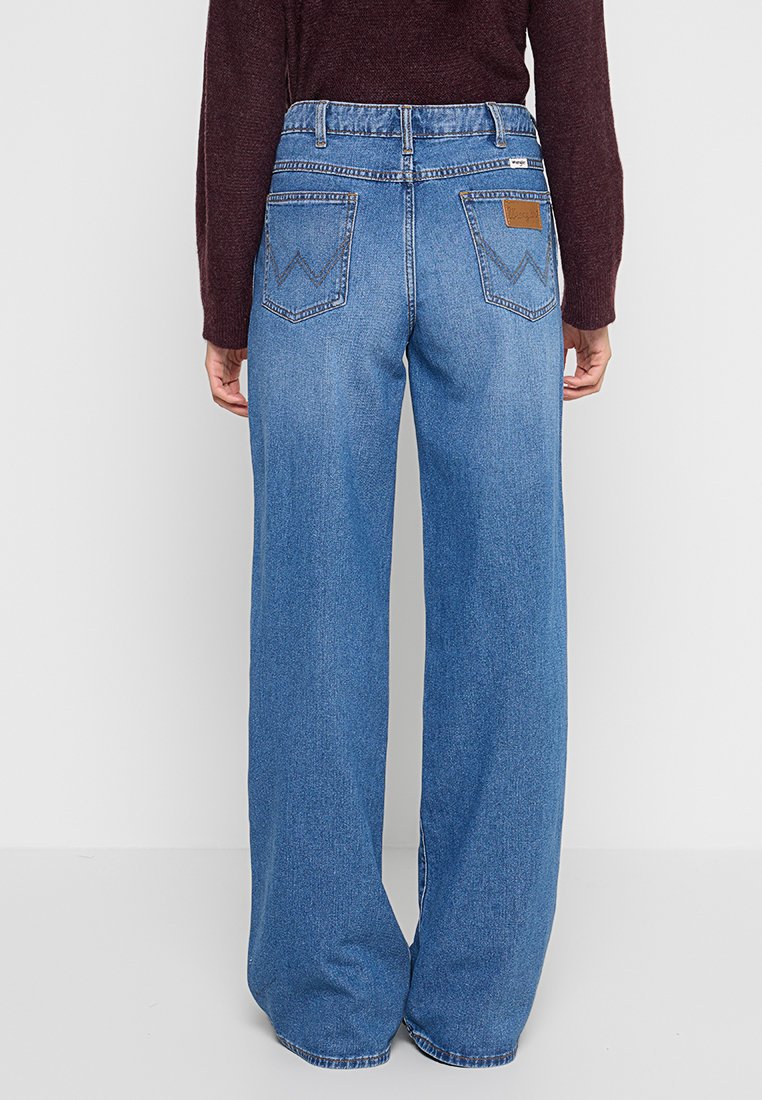 Jeansy z wysokim stanem, szerokie nogawki, niebieski dżins, tylnymi kieszeniami, kontrastującym przeszyciem i brązową skórzaną naszywką w pobliżu pasa.