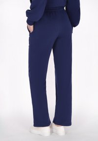 Pantalones de chándal azul marino de corte relajado, con cinturilla elástica y bolsillos laterales, combinados con zapatillas blancas. Textura suave.