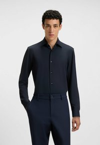 Camicia blu notte a maniche lunghe con colletto classico e chiusura a bottoni, realizzata in tessuto morbido. Abbinata a pantaloni scuri e sartoriali.