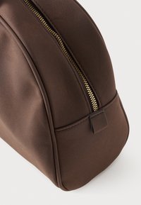 Bolsa sintética castanha com forma arredondada, apresentando um fecho dourado e uma textura suave. Inclui uma pequena alça no fecho.