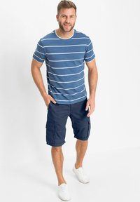 Maglietta di cotone a righe blu con maniche corte abbinata a pantaloni cargo blu scuro. Sneakers bianche completano l'outfit, mostrando uno stile casual.