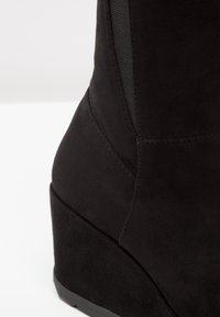 Mustat mokkatossut nilkkapituisilla, joissa on viistokanta, sileä pinta, ompeluyksityiskohdat ja musta joustava sivupaneeli.