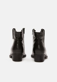 Botines de cuero negro con un acabado suave, cierres de cremallera y un tacón bajo apilado. Presentan un ligero detalle de costura en la parte posterior.