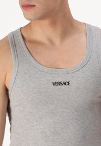 Top sin mangas de color gris con canalé, que presenta un escote redondo y el logo de Versace bordado en negro en el pecho. Tela suave con un ajuste elástico.