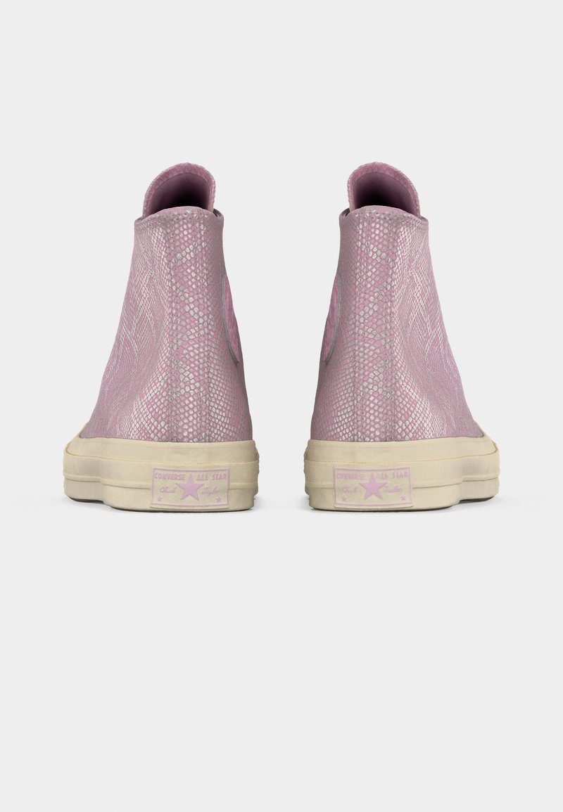 Een paar roze hoge sneakers met een slangenhuidpatroon, beige zolen en het Converse All Star-logo op de hiel, gezien vanaf de achterkant.