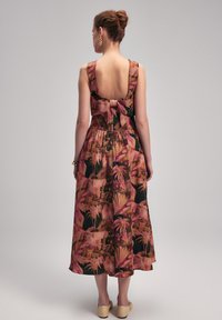 Floral maxi Kleid in Pink, Schwarz und Erdtönen; hat einen tiefen Rückenausschnitt, breite Träger und ein Schleifendetail an der Taille. Glatte Stofftextur.
