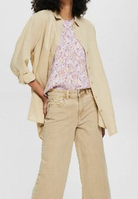 Beige linne skjorta med knappar över en blommönstrad blus i rosa, buren med ljusbeige vida jeans med slitna detaljer.