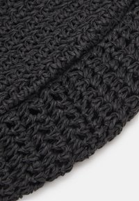 Gros plan sur un tissu noir tissé avec une texture tricotée ouverte et bouclée, et des sections pliées en couches.