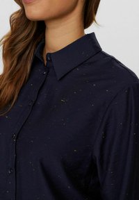 Mørkeblå skjorte med synlige, multikolore sprøjt, knap-op design og klassisk krave. Glat tekstur og løs pasform med knapper.