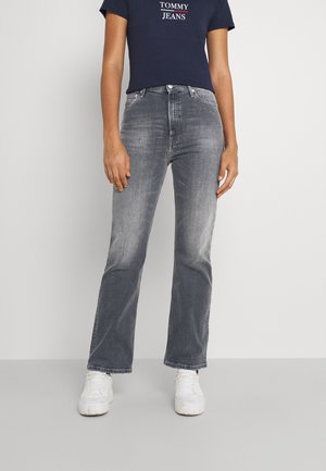 Osoba nosząca wyblakłe szare jeansy o prostych nogawkach, białe sneakersy i granatowy crop top z logo "Tommy Jeans".