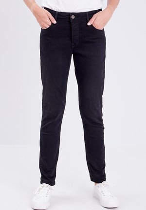 Pantalones negros de corte slim hechos de denim, con cierre de botón, trabillas para cinturón y bolsillos. Combinados con zapatillas blancas.