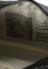 Bolso de lentejuelas negras con interior forrado de tela ligera. En el interior, estampados con la palabra “(IM)PERFECT” en varios estilos. Detalles en plata.