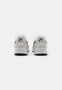 Ténis Nike Air em branco e bege, com um upper em malha e camurça, detalhes em preto e um calcanhar acolchoado com uma unidade de ar visível.