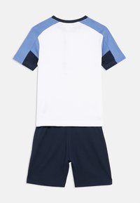 Κοντομάνικο πουκάμισο σε λευκό με μπλε και ναυτικό μπλε λεπτομέρειες· συνδυασμένο με ναυτικό μπλε σορτς. Κατασκευασμένο από μαλακό, ελαφρύ ύφασμα, κατάλληλο για καθημερινή χρήση.