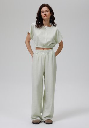Top scurt de culoare verde deschis, cu mâneci scurte și tiv elastic, asortat cu pantaloni largi ce au un talie elastică și o textură netedă.