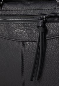 Sac à main en cuir noir avec une surface texturée, une fermeture éclair et une plaque logo. Les détails incluent un long tirette en cuir pour la fermeture éclair et des coutures.