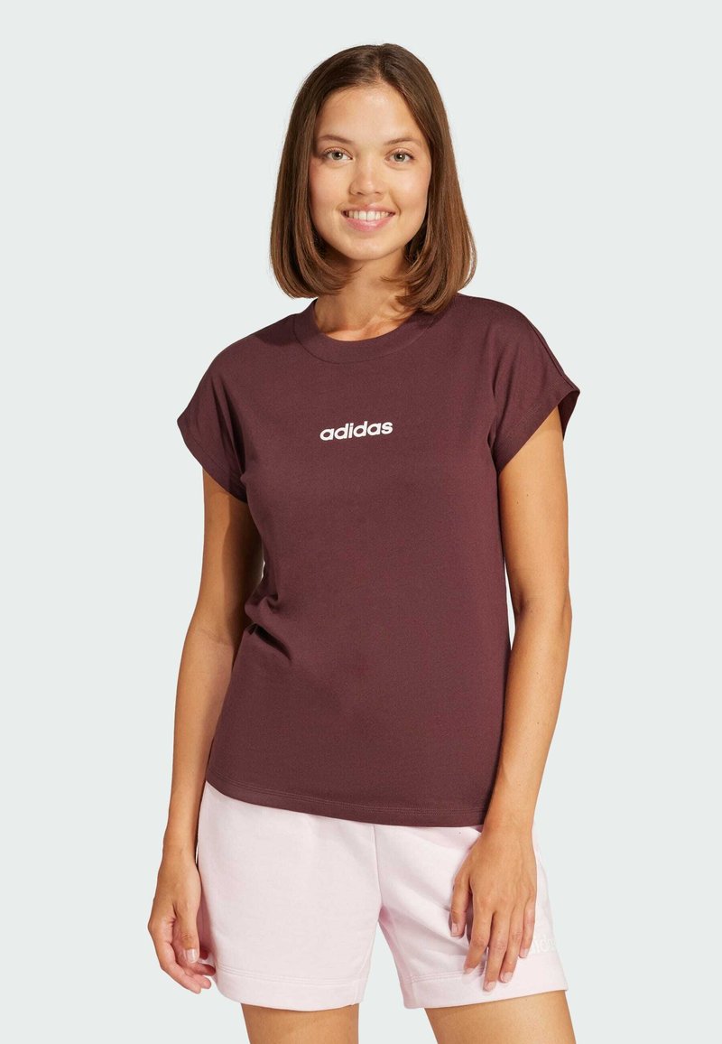 T-shirt in cotone bordeaux con maniche arrotolate e logo "adidas" bianco sul petto, abbinato a pantaloni corti rosa chiaro. Tessuto morbido, vestibilità casual.