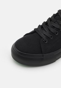 Black canvas sneaker featuring a textured upper, round toe, sturdy rubber sole, and matching black laces with metal eyelets.