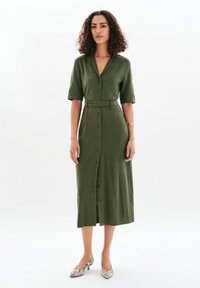 Robe midi vert olive avec manches courtes, col, boutons sur le devant et une ceinture assortie. Chaussures imprimées avec un motif reptilien.