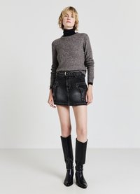 Gray knit sweater paired with a black denim mini skirt featuring front pockets and a studded belt. Worn with tall, black leather boots.