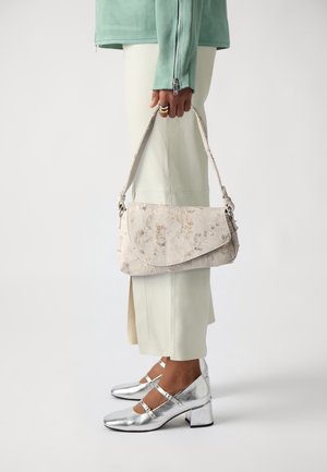 Henkilö, jolla on päällään mintunvihreä takki, kermaisen värinen hame, hopeanväriset Mary Jane -korkokengät, ja joka pitää beigeä, tekstuurillista käsilaukkua sen hihnasta sivullaan.