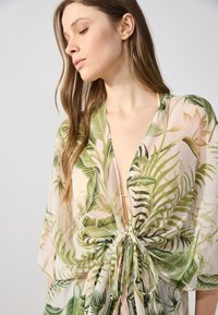 Kevyt, läpikuultava kimono, jossa on trooppinen lehtikuvio vihreänä ja pinkkinä. Ominaisuuksia ovat syvä V-pääntie ja nauhakiinnitys vyötäröllä.
