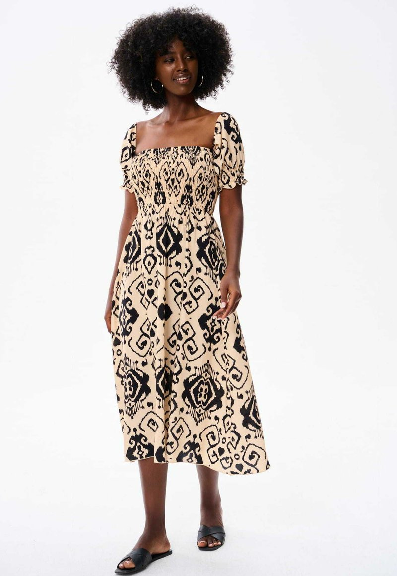 Zwart en beige patroonjurk met een vierkante halslijn, korte puffmouwen en een gerimpelde bodice. Midi-lengte met een vloeiende rok.